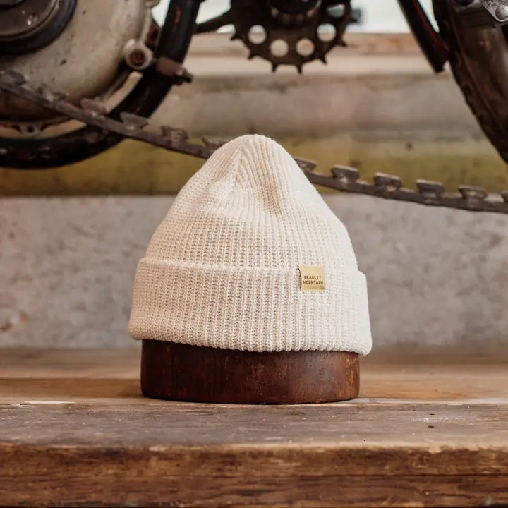 Cream knit beanie with a folded brim, styled for warmth and rugged simplicity against an industrial backdrop