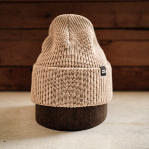 Neutral sand-colored knit beanie with a folded brim, offering cozy warmth and minimalist outdoor style