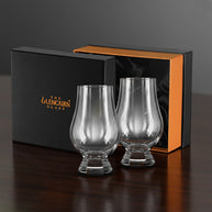 Two Glencairn whisky glasses in front of a branded box on a dark surface.