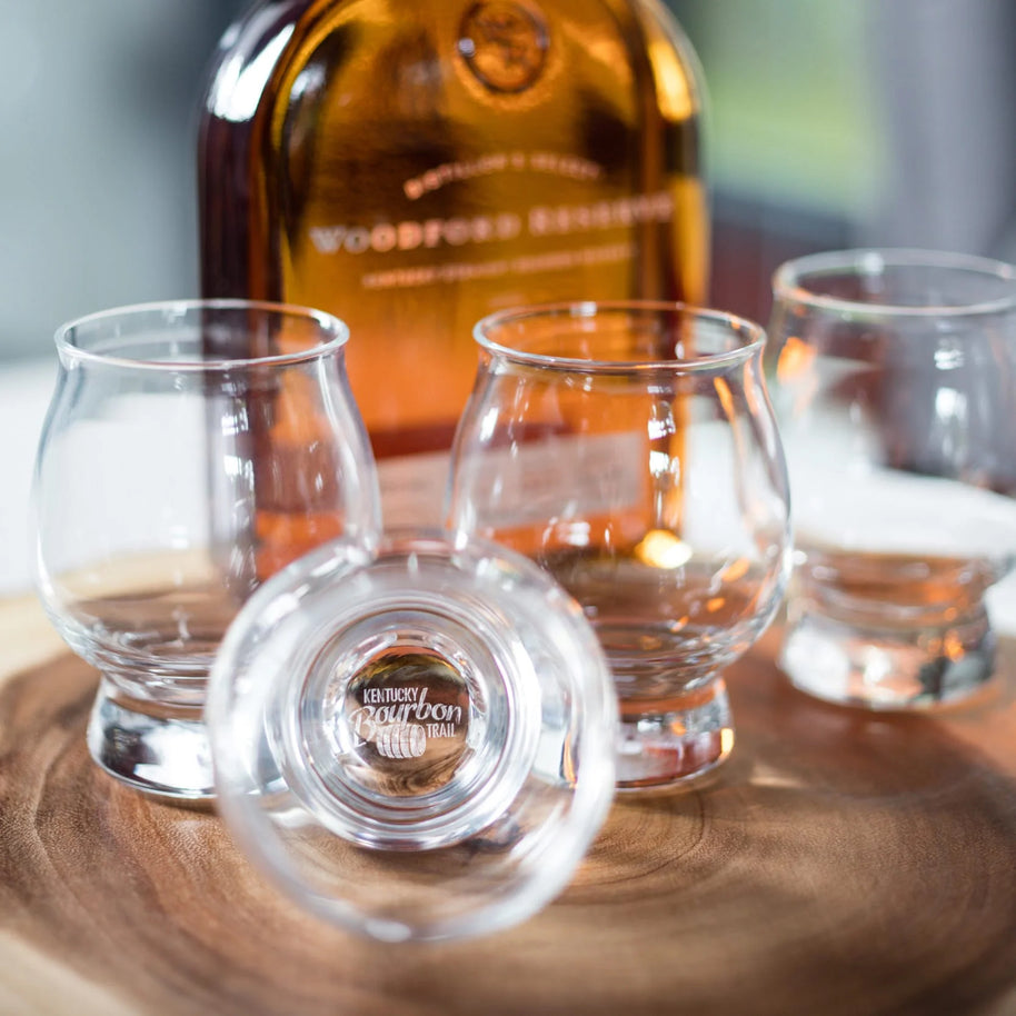 Whiskey glasses on a wood surface with a bourbon bottle, featuring engraved “Kentucky Bourbon Trail” detail on the base