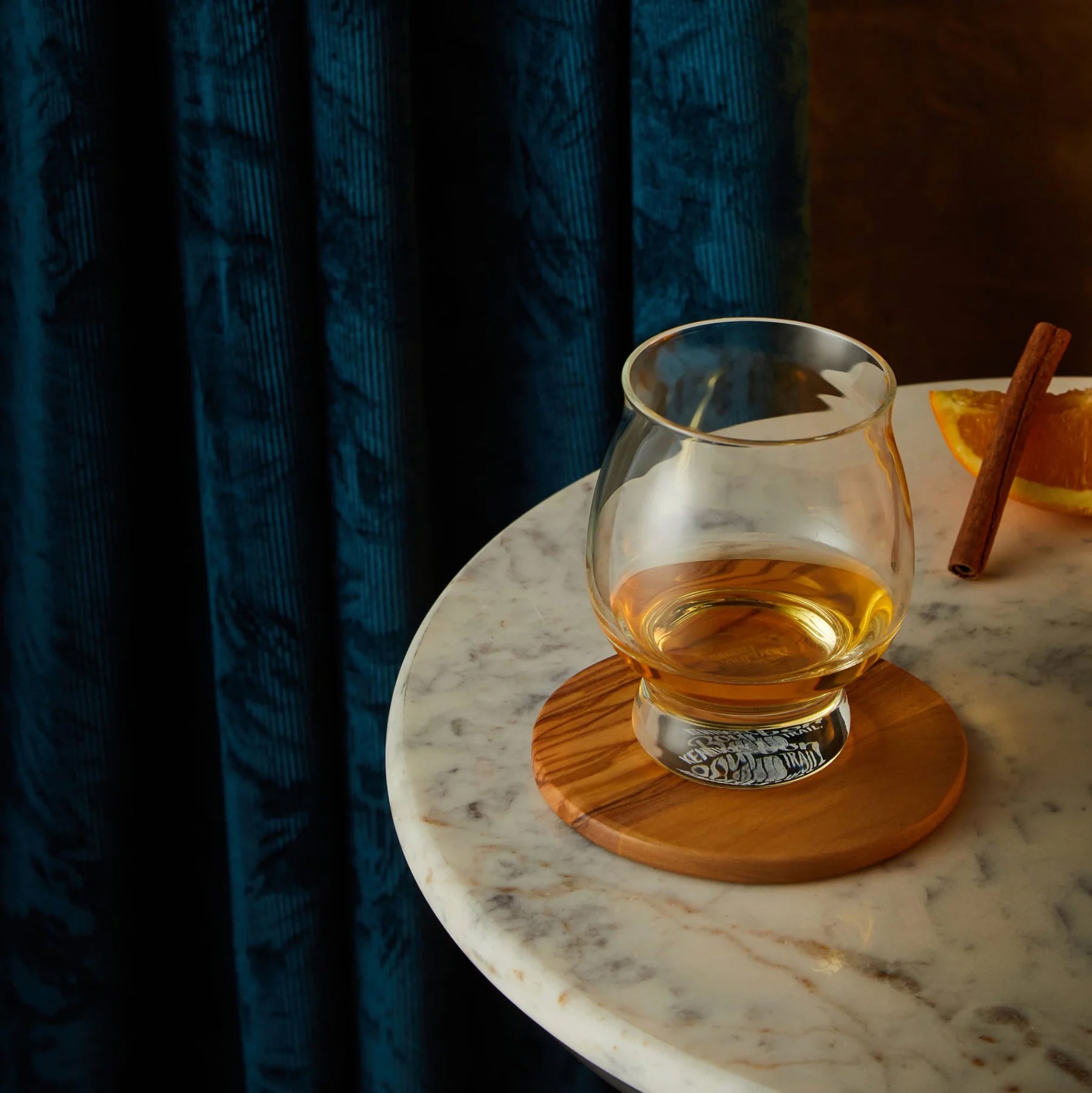 Whiskey glass with a neat pour on a wood coaster, styled with orange and cinnamon for a cozy, elegant drinking scene