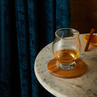 Whiskey glass with a neat pour on a wood coaster, styled with orange and cinnamon for a cozy, elegant drinking scene