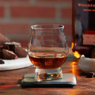 Whiskey glass with a rich amber pour on a stone coaster, styled beside bourbon and chocolate for a refined pairing