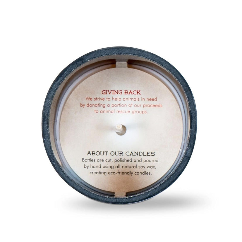 Top view of a candle with a printed message inside the container. The text reads: “GIVING BACK: We strive to help animals in need by donating a portion of our proceeds to animal rescue groups. ABOUT OUR CANDLES: Bottles are cut, polished and poured by hand using all natural soy wax, creating eco-friendly candles.”