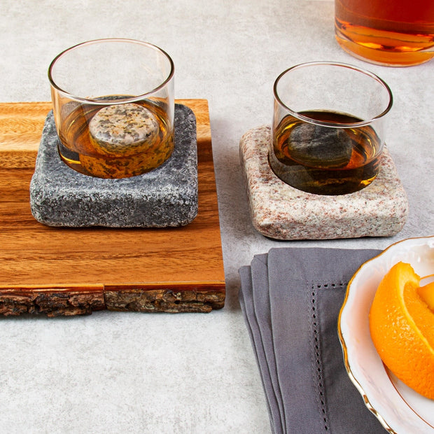 Whiskey glasses in granite bases with chilling stones, styled with citrus and wood accents for a refined serving setup