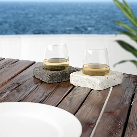 Two glasses of white wine on stone coasters with a scenic ocean view.