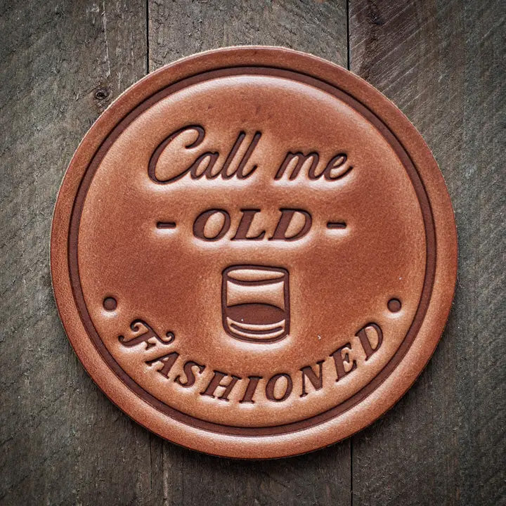 Round leather coaster stamped with the phrase ‘Call me Old Fashioned’ and a whiskey glass graphic, rustic barware design