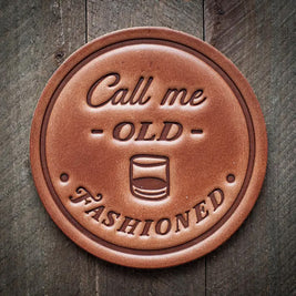 Round leather coaster stamped with the phrase ‘Call me Old Fashioned’ and a whiskey glass graphic, rustic barware design