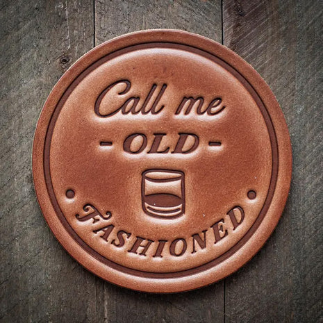 Round leather coaster stamped with the phrase ‘Call me Old Fashioned’ and a whiskey glass graphic, rustic barware design
