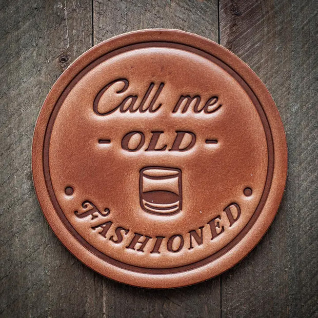 Round leather coaster stamped with the phrase ‘Call me Old Fashioned’ and a whiskey glass graphic, rustic barware design