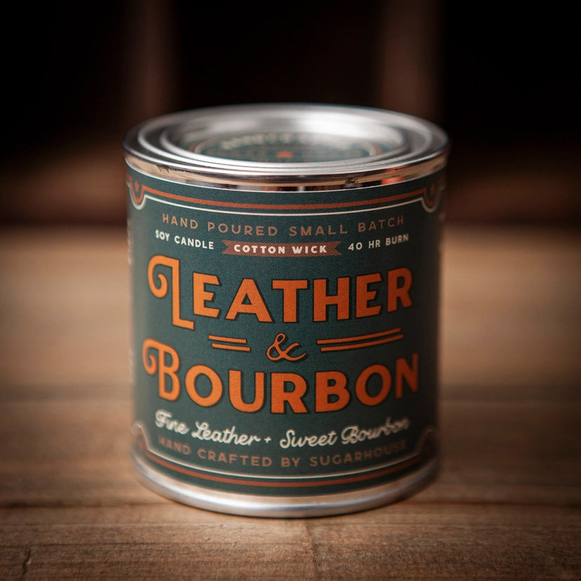 Leather & Bourbon soy candle by Sugarhouse in 8oz metal tin. Dark green vintage-style label with orange lettering: Hand poured small batch, cotton wick, 40 hour burn, fine leather + sweet bourbon scent