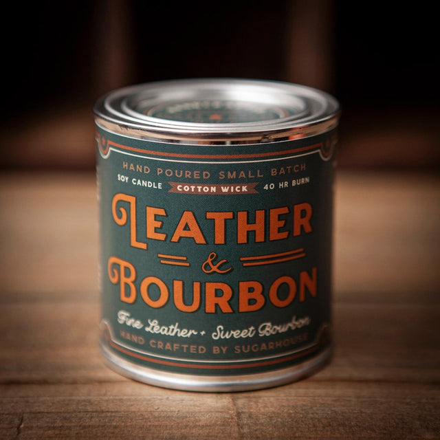 Leather & Bourbon soy candle by Sugarhouse in 8oz metal tin. Dark green vintage-style label with orange lettering: Hand poured small batch, cotton wick, 40 hour burn, fine leather + sweet bourbon scent