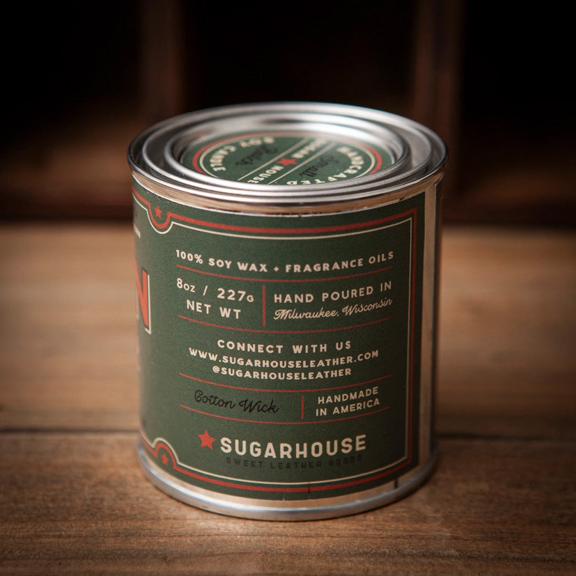 Back of Sugarhouse Cabin Fever soy candle tin. Label details: 100% soy wax + fragrance oils, 8oz / 227g, hand poured in Milwaukee, Wisconsin, cotton wick, handmade in America. Sugarhouse branding and website included