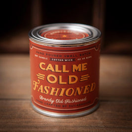 Sugarhouse candle tin with a deep red-orange label and silver lid. The front reads “Call Me Old Fashioned” in bold yellow and gold lettering, with “Brandy Old Fashioned” and “Hand Crafted by Sugarhouse” below. Additional text highlights “Hand Poured Small Batch,” “Soy Candle,” “Cotton Wick,” and “40 HR Burn.”