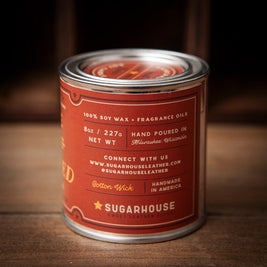 Sugarhouse candle tin with a deep red label and silver lid. The label text reads “100% Soy Wax + Fragrance Oils,” “8oz / 227g Net Wt,” “Hand Poured in Milwaukee, Wisconsin,” “Cotton Wick,” and “Handmade in America.” Branding at the bottom includes “Sugarhouse Sweet Leather Goods” with a small star icon.