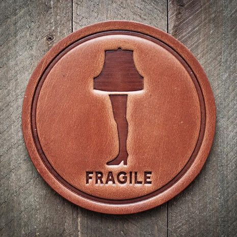 Round leather coaster embossed with the leg lamp design and the word ‘Fragile’ below, rustic barware style