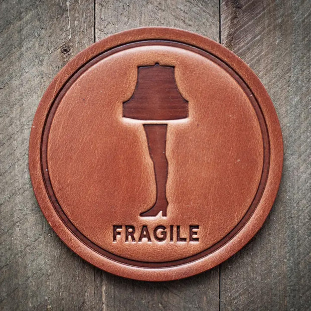 Round leather coaster embossed with the leg lamp design and the word ‘Fragile’ below, rustic barware style