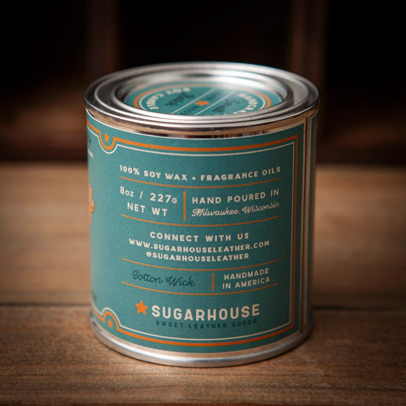 Sugarhouse candle tin with teal label and silver lid. The back of the label lists details: “100% Soy Wax + Fragrance Oils,” “8oz / 227g Net Wt,” “Hand Poured in Milwaukee, Wisconsin,” “Cotton Wick,” “Handmade in America,” plus contact information and the Sugarhouse logo with an orange star