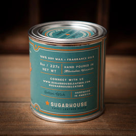 Sugarhouse candle tin with teal label and silver lid. The back of the label lists details: “100% Soy Wax + Fragrance Oils,” “8oz / 227g Net Wt,” “Hand Poured in Milwaukee, Wisconsin,” “Cotton Wick,” “Handmade in America,” plus contact information and the Sugarhouse logo with an orange star
