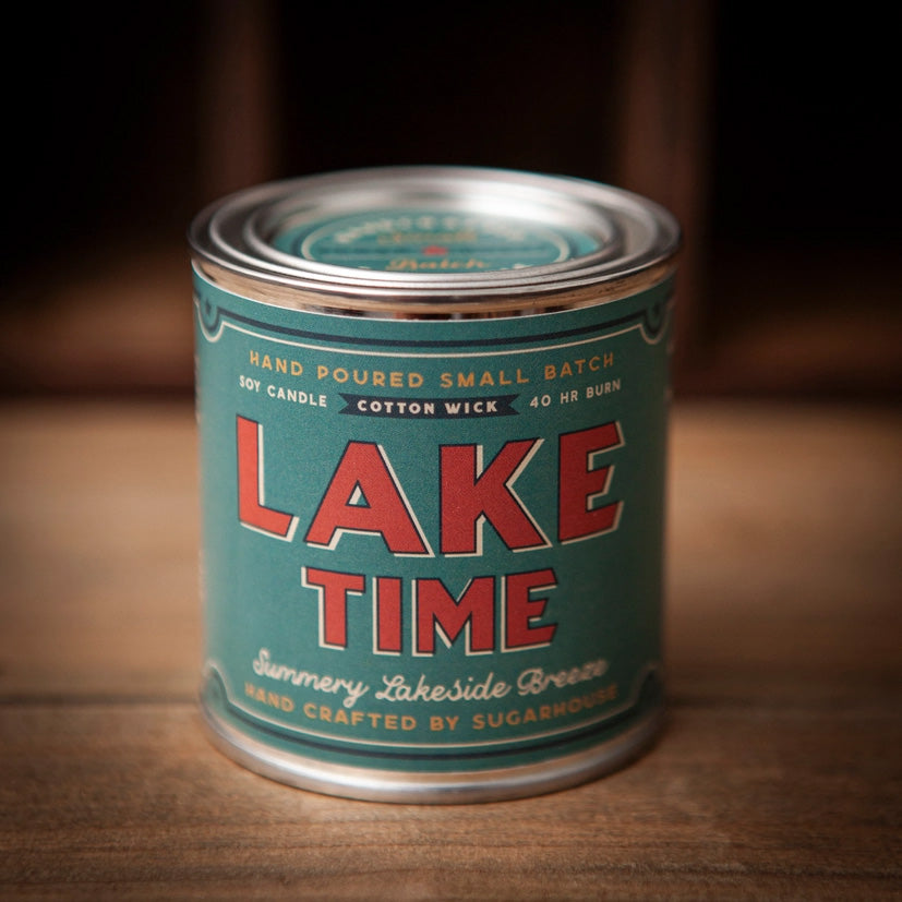Sugarhouse candle tin with teal label and silver lid. The label features bold red text reading “Lake Time,” with smaller text “Summery Lakeside Breeze,” “Hand Poured Small Batch Soy Candle,” “Cotton Wick,” “40 Hr Burn,” and “Hand Crafted by Sugarhouse.”