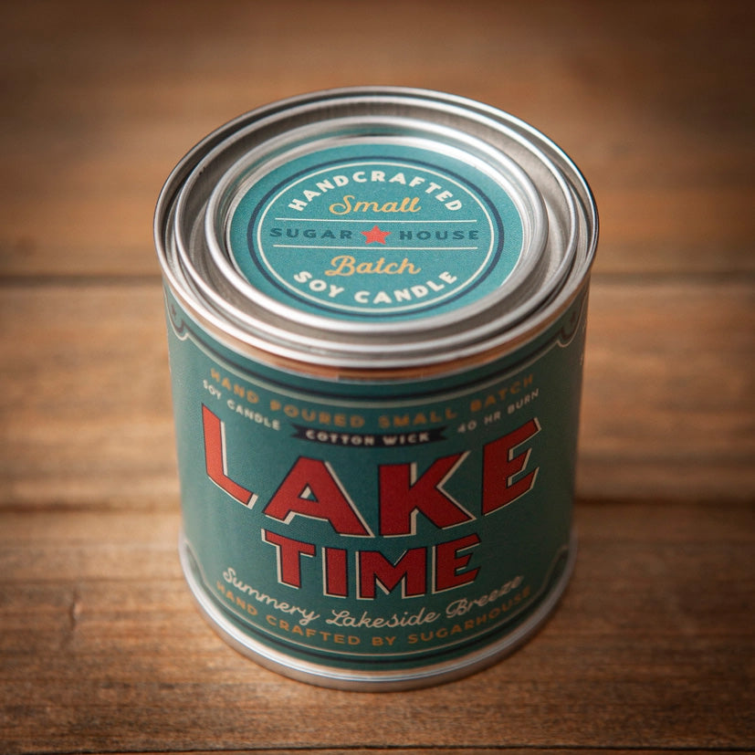Sugarhouse candle tin with teal label and silver lid. The label reads “Lake Time” in large red letters, with smaller text “Summery Lakeside Breeze,” “Hand Poured Small Batch Soy Candle,” “Cotton Wick,” “40-hour Burn,” and “Hand Crafted by Sugarhouse.”