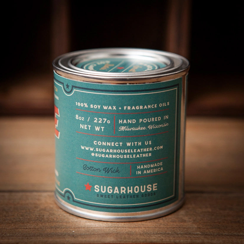 Sugarhouse candle tin with a dark green label showing product details: “100% Soy Wax + Fragrance Oils,” “8oz / 227g Net Wt,” “Hand Poured in Milwaukee, Wisconsin,” “Cotton Wick,” and “Handmade in America.”