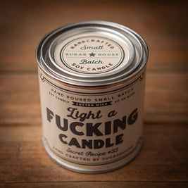 Sugarhouse candle tin labeled “Light a Fucking Candle” in bold text. Cream-colored label with black and gray lettering, featuring phrases like “Hand Poured Small Batch Soy Candle,” “Cotton Wick, 40-hour Burn, and “Secret Recipe #33
