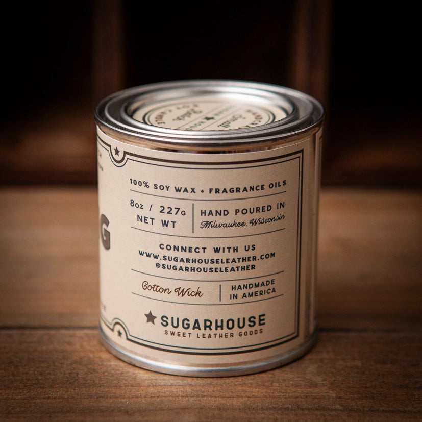 Back label of a Sugarhouse soy candle tin in cream color. Text reads “100% Soy Wax + Fragrance Oils,” “8oz / 227g,” “Hand Poured in Milwaukee, Wisconsin.” Includes contact info, “Cotton Wick,” “Handmade in America,” and “Sugarhouse Sweet Leather Goods