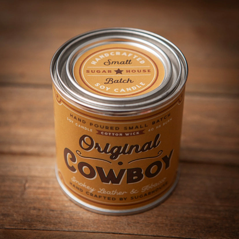 Yellow Sugarhouse soy candle tin labeled “Original Cowboy.” The design features bold vintage typography with the scent described as “Smokey Leather & Tobacco.” The lid reads “Handcrafted Small Batch Soy Candle