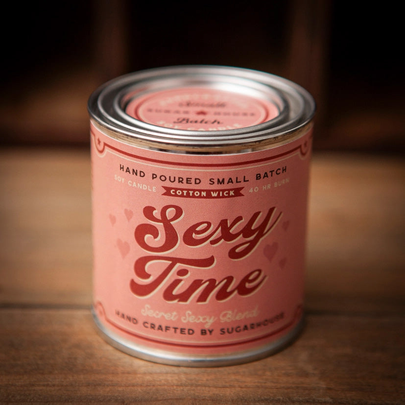 Pink Sugarhouse soy candle labeled “Sexy Time – Secret Sexy Blend,” with small heart graphics, in a vintage-style tin can with a metal lid, sitting on a wooden surface