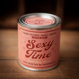 Pink Sugarhouse soy candle labeled “Sexy Time – Secret Sexy Blend,” with small heart graphics, in a vintage-style tin can with a metal lid, sitting on a wooden surface