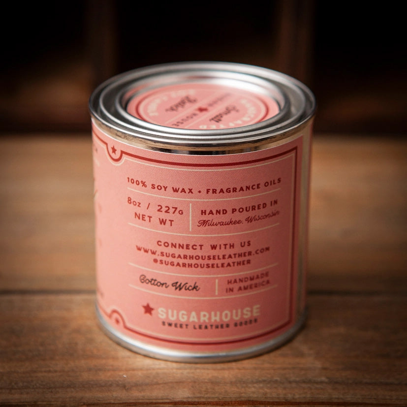 Back view of Sugarhouse Sexy Time soy candle tin. Label text: 100% soy wax with fragrance oils, 8oz / 227g, hand poured in Milwaukee, Wisconsin. Cotton wick. Handmade in America. Sugarhouse Sweet Leather Goods branding with website and social handles