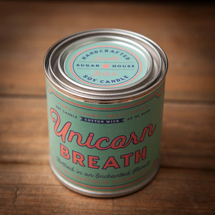 Front view of Unicorn Breath soy candle tin. Label reads: Unicorn Breath – Hand-poured small batch soy candle, cotton wick, 40-hour burn. Designed in pastel mint green and pink with retro lettering