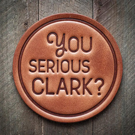 Round leather coaster with embossed phrase ‘You Serious Clark?’ for a rustic, humorous holiday touch.
