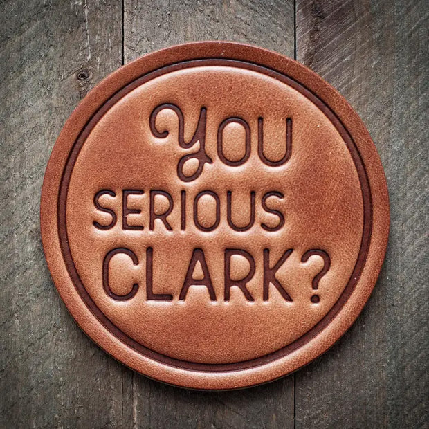 Round leather coaster with embossed phrase ‘You Serious Clark?’ for a rustic, humorous holiday touch.