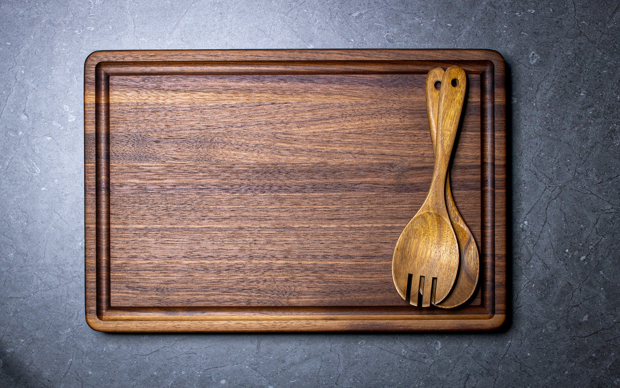 Wooden cutting board with a wooden spoon and fork on a gray surface
