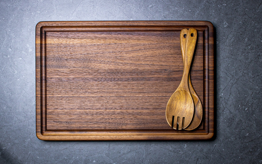 Wooden cutting board with a wooden spoon and fork on a gray surface
