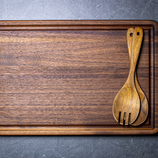 Wooden cutting board with a wooden spoon and fork on a gray surface