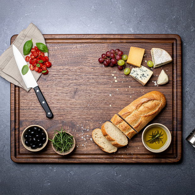 Wooden cutting board with bread, cheese, fruits, and herbs on a gray surface